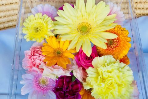 アクリルケースに納められた黄色いガーベラなどの色とりどりの花々。