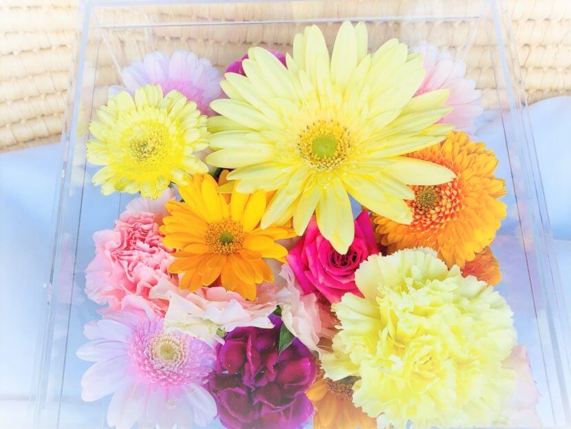 アクリルのケースに入ったオレンジや黄色のガーベラやカーネーションなどの花々